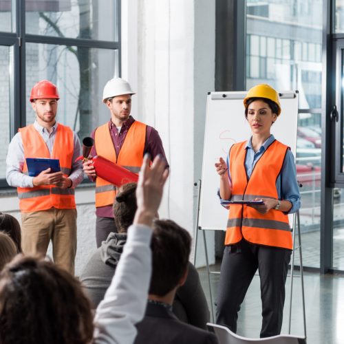 selective focus of firemen in helmets standing near attractive firefighter giving talk near white